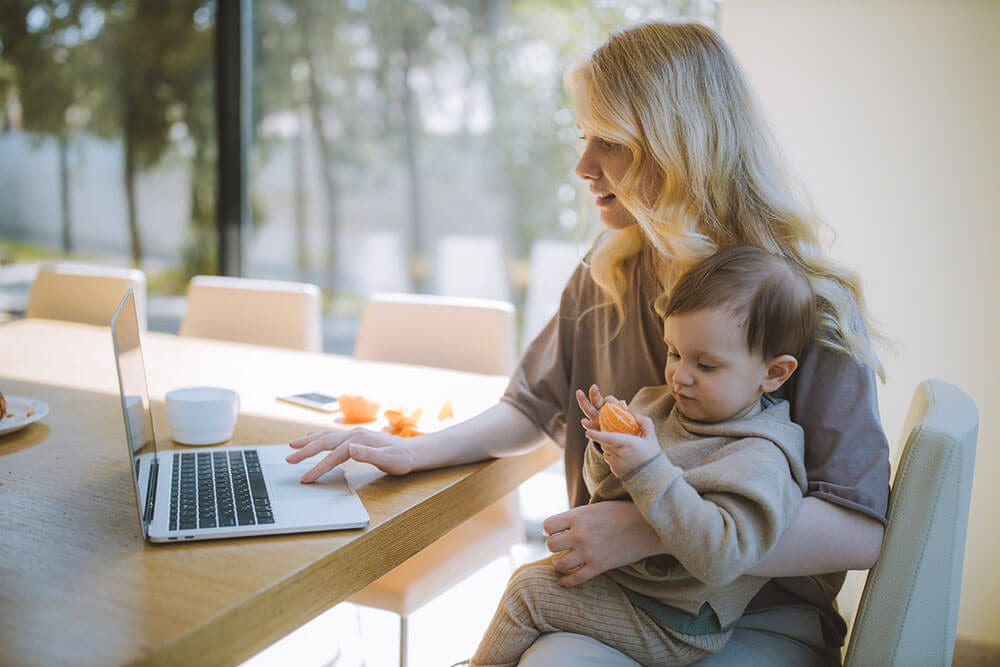 Vrouw met baby op schoot achter laptop geboortekaartjes aan het bestellen